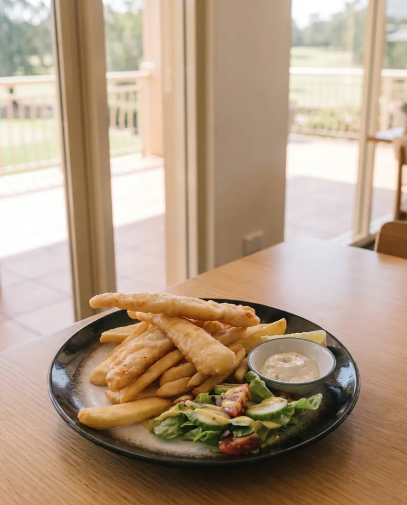 Tempura flathead tails with fries, garden salad, tartare and lemon, on a table by the glass doors